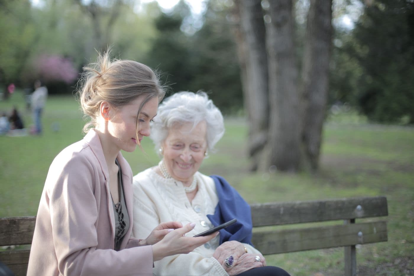Adult daughter helping her senior mother use a tablet in a sunny park