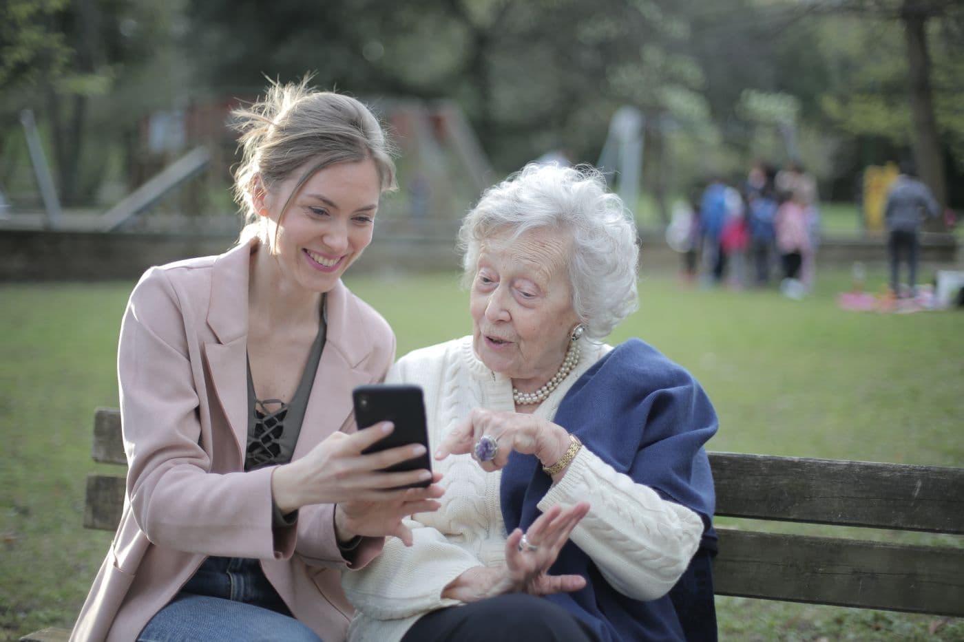 Adult daughter and senior mother smiling together outdoors with a phone