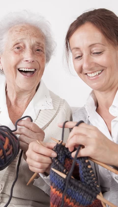 Caregiver and resident knitting together and smiling